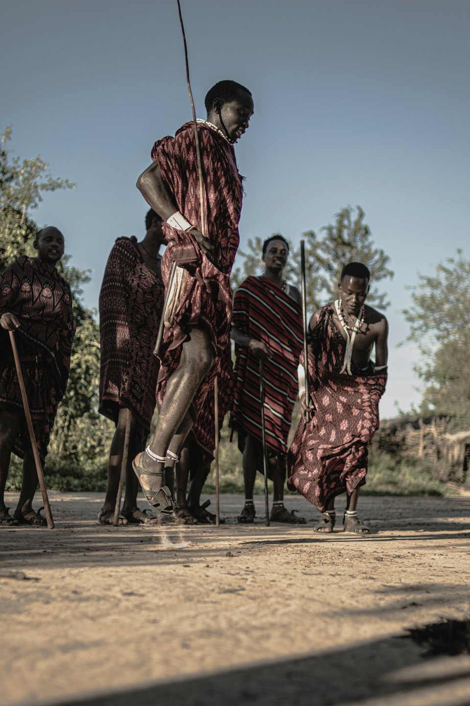 Maasai men performing a traditional jumping dance on dusty ground.
